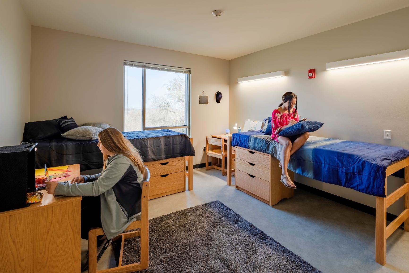 Inside of dorm room with two students studying. Viewing window, two beds, two desks