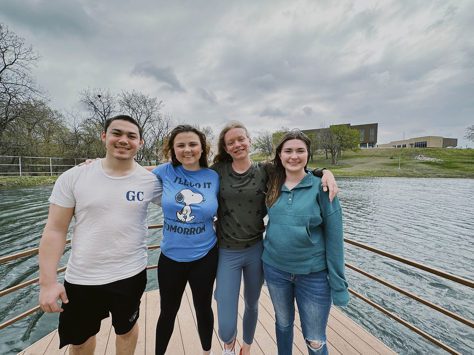 Four students with arms over shoulders standing in front of pond