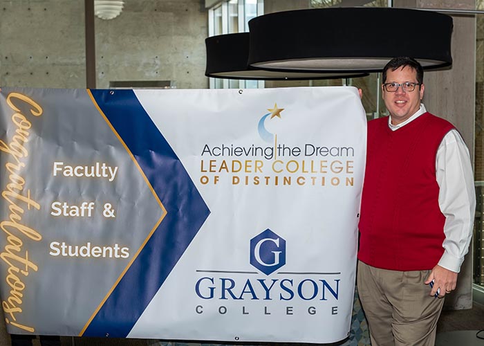 Grayson College President Dr. McMillen holding banner commemorating the Leader College of Distinction Award