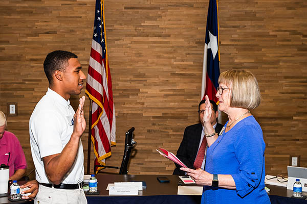 Student in business attire being sword in in front of Board members