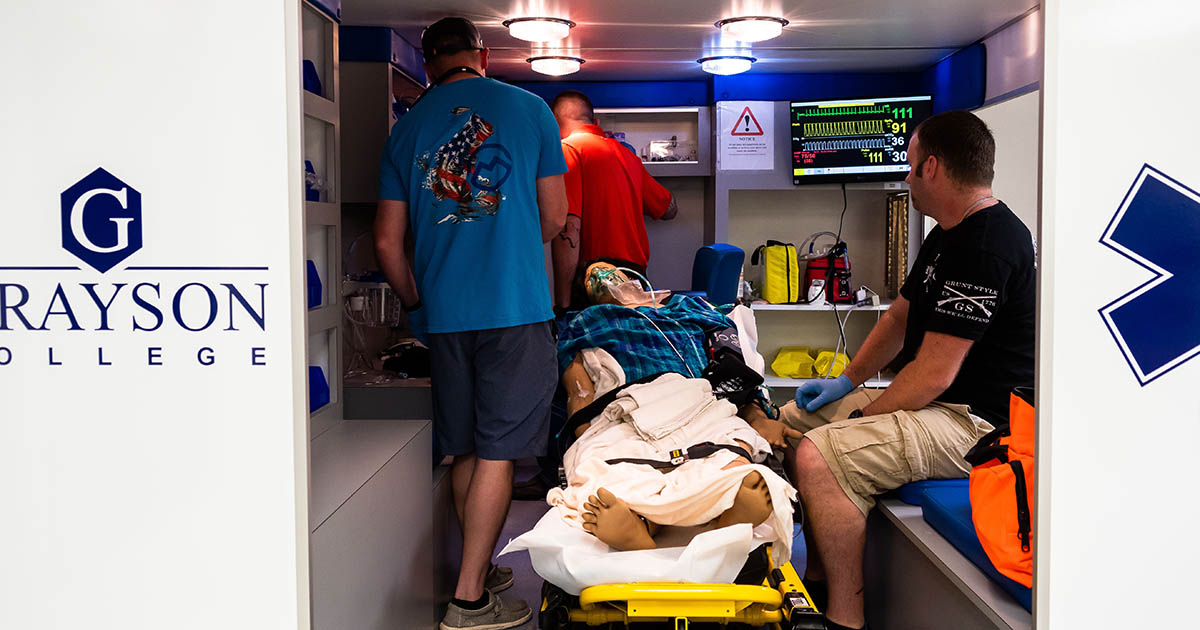 three individuals in a simulated ambulance providing care to a medical dummy
