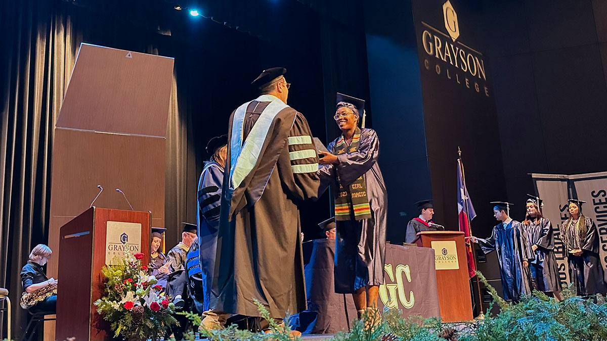 Man in academic garb delivering diploma to student in regalia