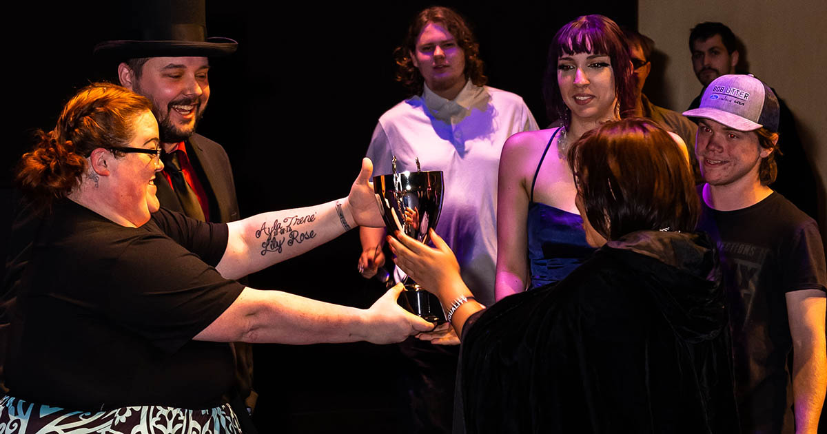 Woman hands over a golden trophy to students waiting in line to receive awards