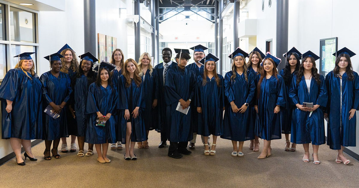 Line of dual students posing for a photograph wearing graduation regalia