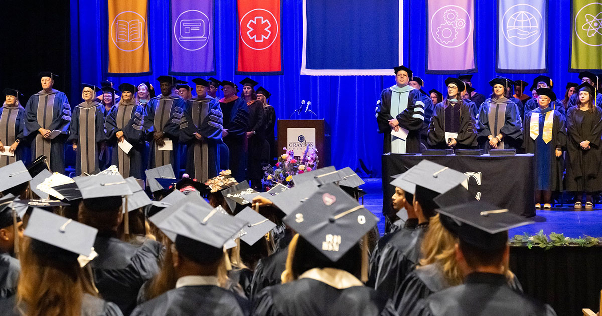 President Jeremy McMillen on stage with faculty members during summer commencement ceremony.