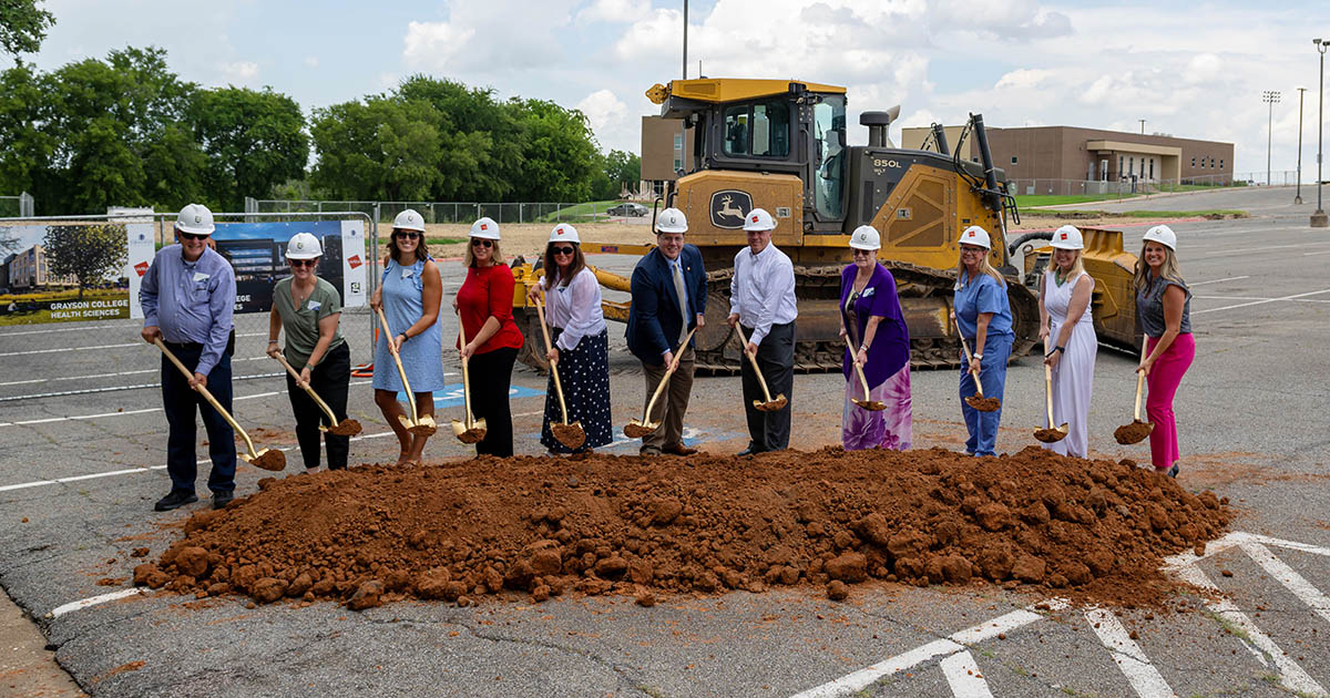 Grayson College Faculty and Staff pose with shovels in front of dirt in front of construction equipment