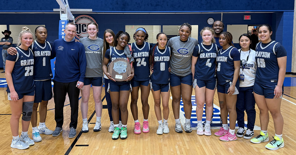 Women's Basketball Team members standing in front of basket with coaches, holding NJCAA plaque